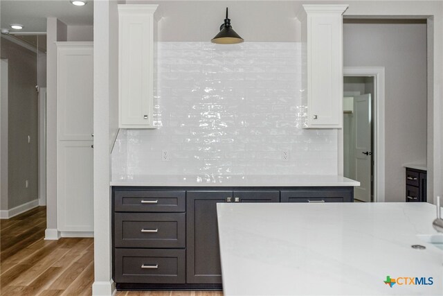 kitchen with backsplash, hanging light fixtures, white cabinetry, and light wood-type flooring