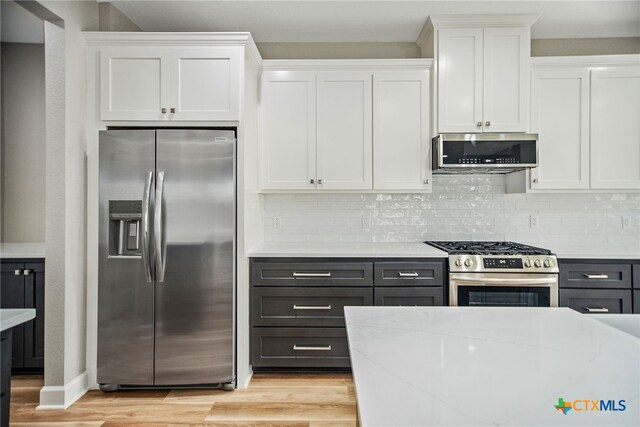 kitchen with light wood-type flooring, white cabinetry, light stone counters, and stainless steel appliances