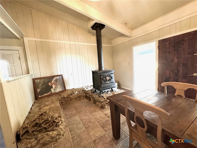 tiled dining space featuring wooden walls, a wood stove, and vaulted ceiling with beams