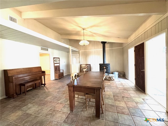 dining area with beamed ceiling, wooden walls, and a wood stove