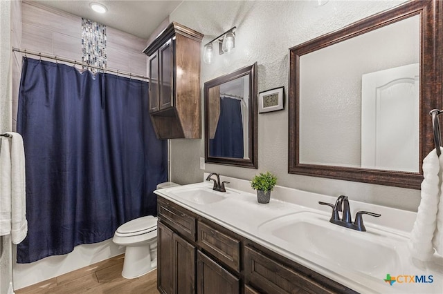 full bathroom with toilet, a textured wall, a sink, and wood finished floors