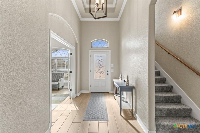 entryway with baseboards, a textured wall, stairway, ornamental molding, and wood finish floors