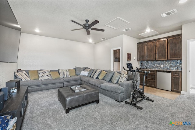 living room with ceiling fan, a textured ceiling, visible vents, and attic access