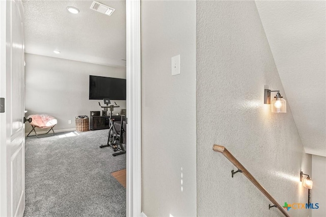 hallway featuring carpet floors, visible vents, a textured wall, and a textured ceiling