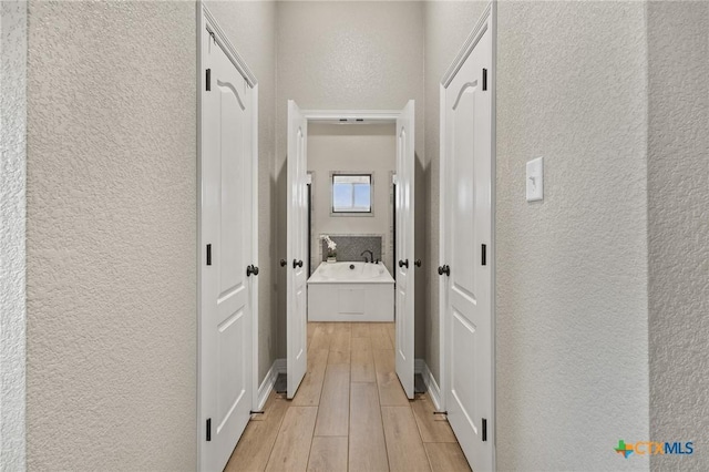 hallway with baseboards, a textured wall, and wood tiled floor