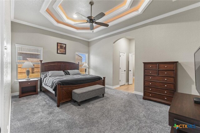 carpeted bedroom with arched walkways, ornamental molding, a raised ceiling, and a ceiling fan