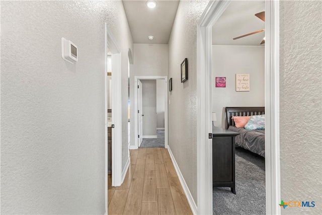 hallway with light wood-type flooring, a textured wall, and baseboards
