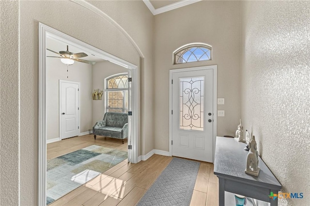 foyer entrance with a ceiling fan, crown molding, baseboards, and wood finished floors