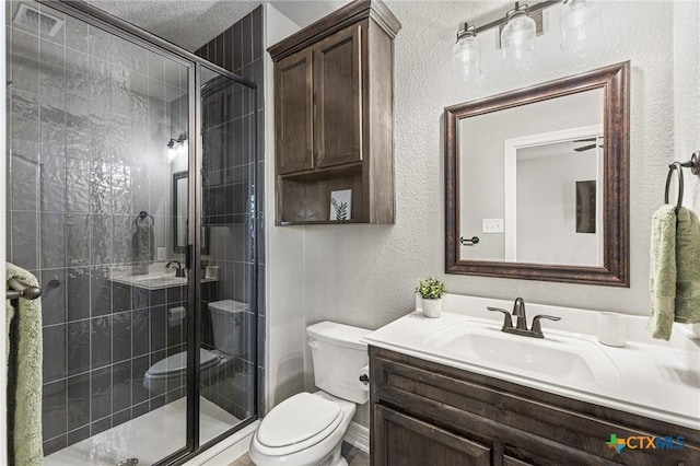 bathroom with a textured wall, vanity, toilet, and a shower stall