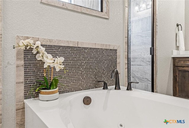 full bath featuring a textured wall, tile walls, a whirlpool tub, and vanity