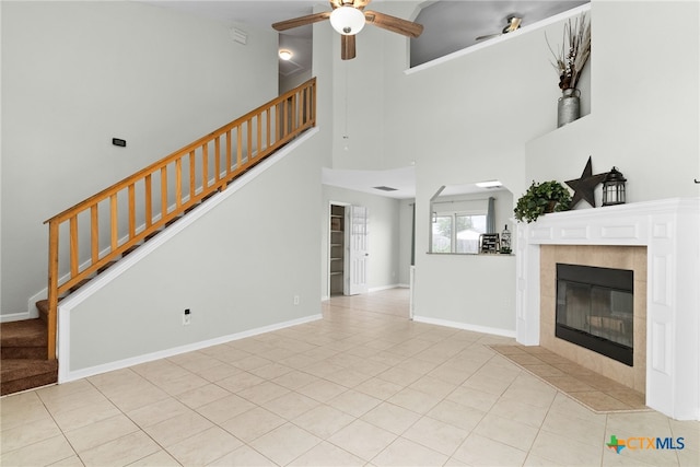 unfurnished living room with a tile fireplace, a towering ceiling, ceiling fan, and light tile patterned flooring