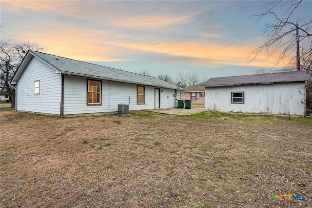 back house at dusk with a yard, central AC, and a patio area