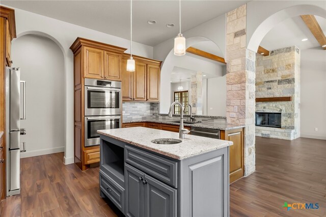 1607 Filtro, New Braunfels, TX 78132 - kitchen featuring stainless steel appliances, arched walkways, light stone countertops, a center island with sink, and beam ceiling