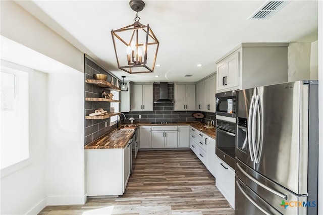 kitchen featuring visible vents, wall chimney range hood, butcher block counters, decorative backsplash, and stainless steel appliances