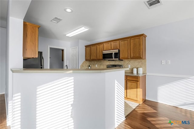 kitchen with tasteful backsplash, appliances with stainless steel finishes, kitchen peninsula, and light wood-type flooring