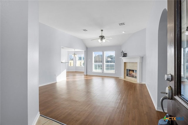 unfurnished living room with vaulted ceiling, a tiled fireplace, ceiling fan with notable chandelier, and light hardwood / wood-style flooring