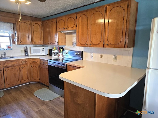 kitchen featuring dark wood-type flooring, backsplash, kitchen peninsula, a textured ceiling, and white appliances