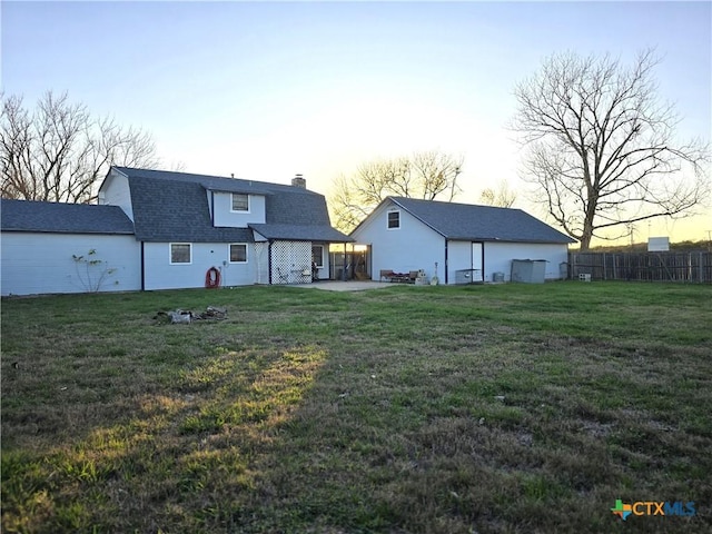 back house at dusk with a lawn and a patio area