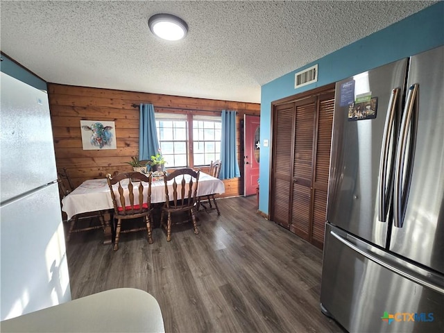 dining space featuring dark hardwood / wood-style floors, a textured ceiling, and wooden walls