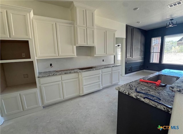 kitchen featuring visible vents, light stone countertops, black electric stovetop, a textured ceiling, and concrete floors