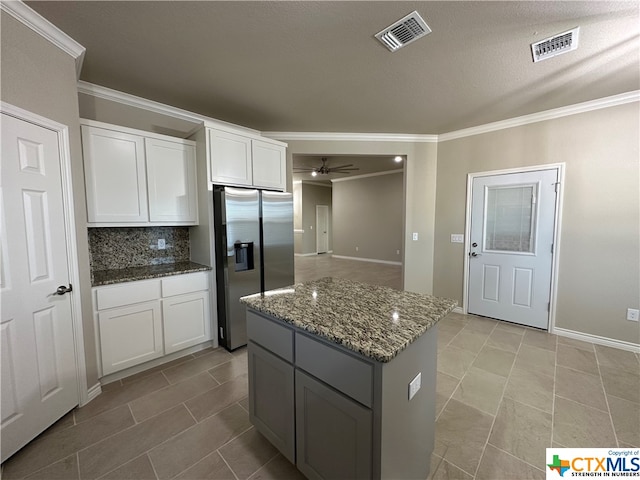 kitchen with white cabinetry, stainless steel refrigerator with ice dispenser, decorative backsplash, dark stone countertops, and a center island