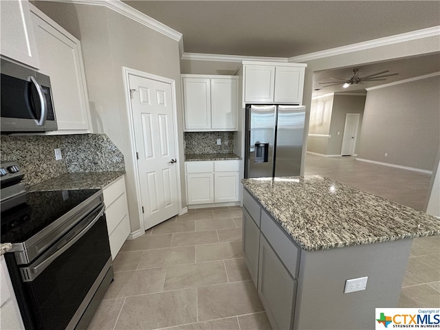 kitchen with stainless steel appliances, light stone counters, a center island, white cabinets, and decorative backsplash