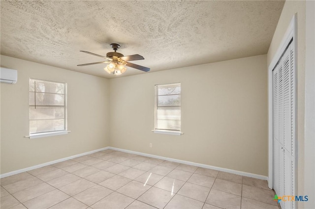 unfurnished bedroom featuring a textured ceiling, light tile patterned floors, an AC wall unit, a closet, and ceiling fan