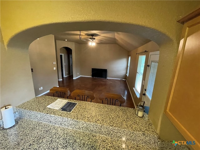 kitchen with ceiling fan, light stone countertops, and lofted ceiling