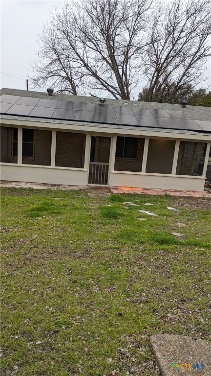 back of property featuring a sunroom, solar panels, and a yard