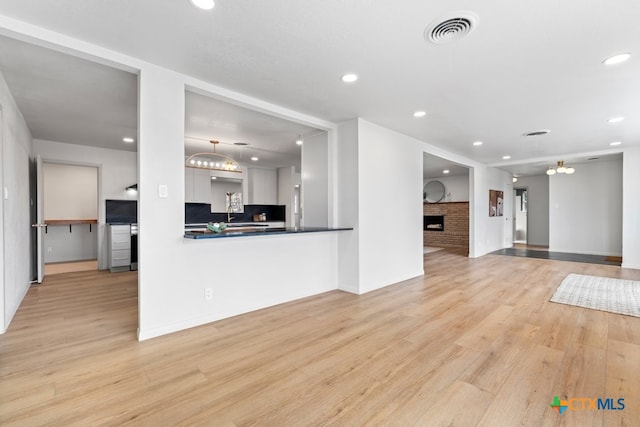 kitchen with decorative light fixtures, a brick fireplace, white cabinets, light hardwood / wood-style floors, and backsplash