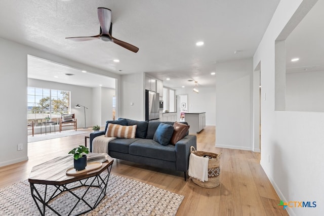 living room with a textured ceiling, light hardwood / wood-style floors, and ceiling fan