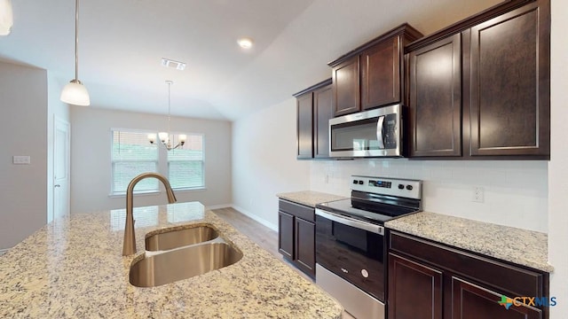 kitchen with light stone counters, sink, stainless steel appliances, and hanging light fixtures