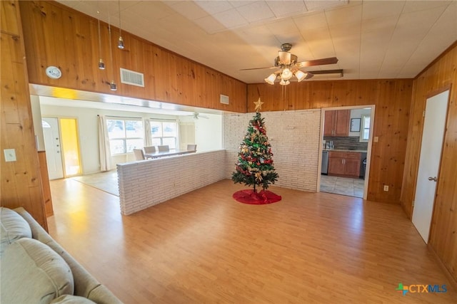 dining space with light hardwood / wood-style flooring, ceiling fan, wooden walls, and brick wall