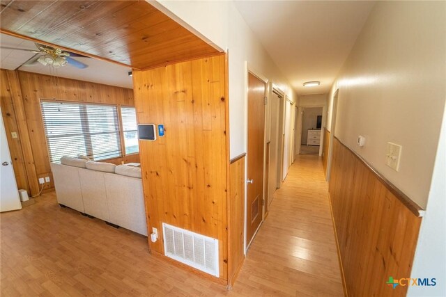 corridor with wood walls, light hardwood / wood-style flooring, and wooden ceiling