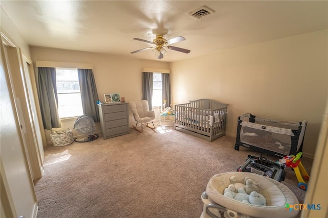 carpeted bedroom with ceiling fan and a nursery area