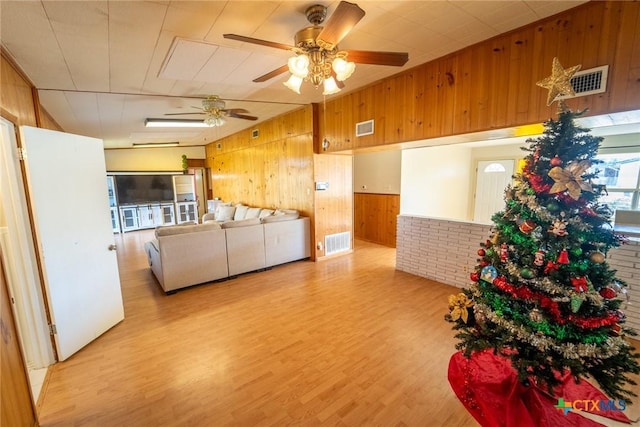 living room featuring ceiling fan, light wood-type flooring, and wooden walls