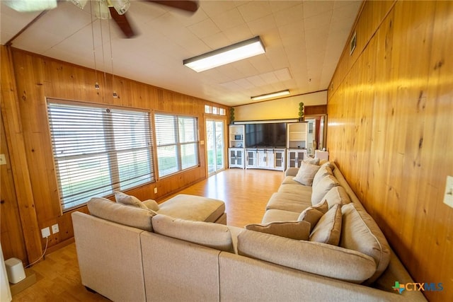 living room with ceiling fan, light hardwood / wood-style flooring, a wealth of natural light, and wood walls