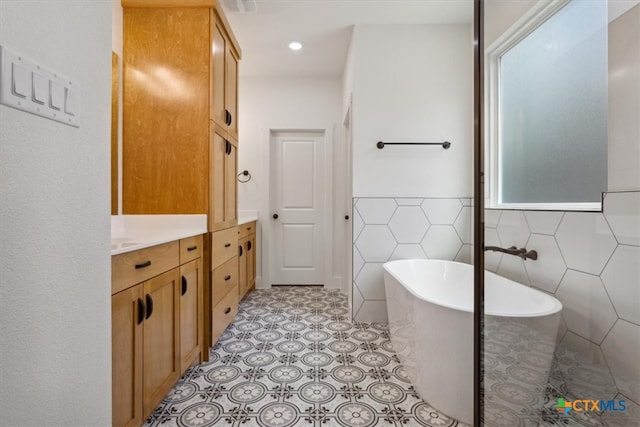 bathroom with tile walls, tile patterned flooring, a bath, and vanity