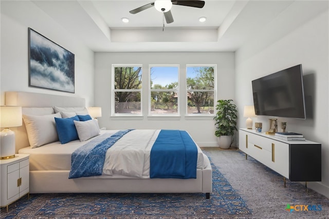 bedroom with dark colored carpet, ceiling fan, and a tray ceiling