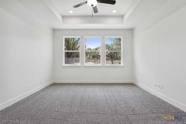 carpeted empty room featuring ceiling fan and a raised ceiling