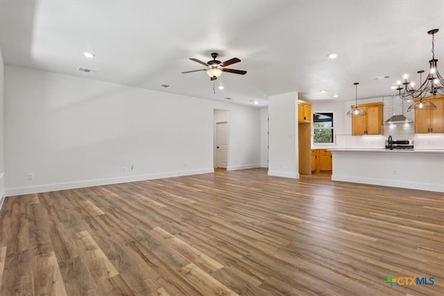 unfurnished living room featuring ceiling fan with notable chandelier, hardwood / wood-style flooring, and sink