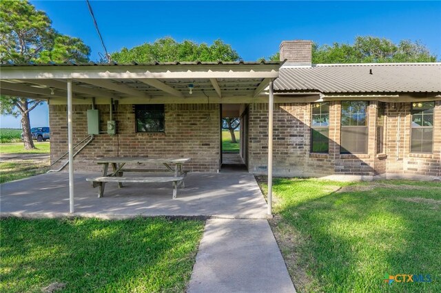 exterior space featuring brick siding, a front yard, a patio area, and a chimney