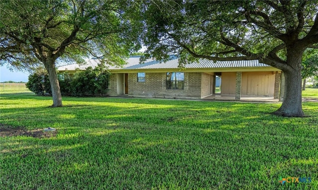 rear view of house with brick siding, a lawn, and metal roof
