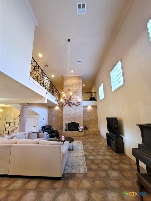 living area with a towering ceiling, a brick fireplace, visible vents, and crown molding