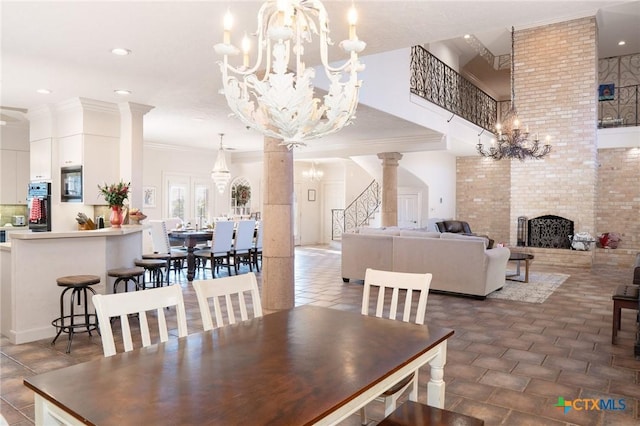 dining room featuring an inviting chandelier, decorative columns, a brick fireplace, and crown molding