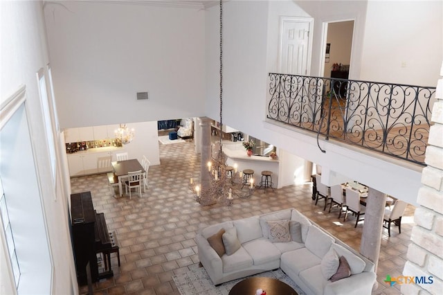 living room featuring a towering ceiling, stairs, visible vents, and a notable chandelier