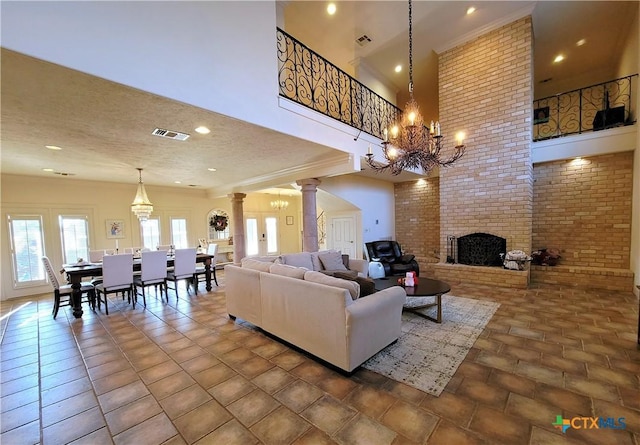 living area with a brick fireplace, visible vents, decorative columns, and a towering ceiling