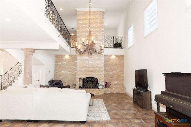 living area featuring stairs, ornamental molding, a brick fireplace, decorative columns, and an inviting chandelier