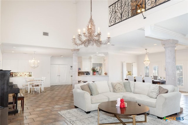 living area with ornate columns, visible vents, crown molding, and an inviting chandelier