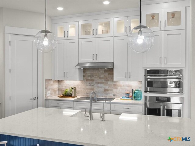 105 Monterey Oak Trl, Georgetown, TX 78628 - kitchen with under cabinet range hood, black electric cooktop, white cabinetry, backsplash, and decorative light fixtures